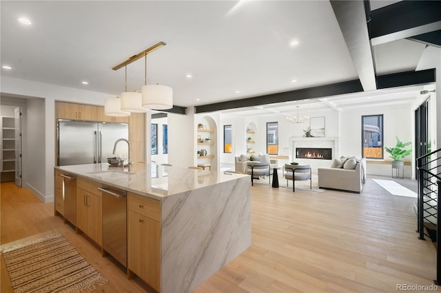 kitchen with a large island, stainless steel appliances, light stone counters, pendant lighting, and light wood-type flooring