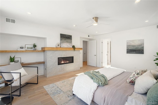 bedroom with a tile fireplace, light hardwood / wood-style floors, and ceiling fan