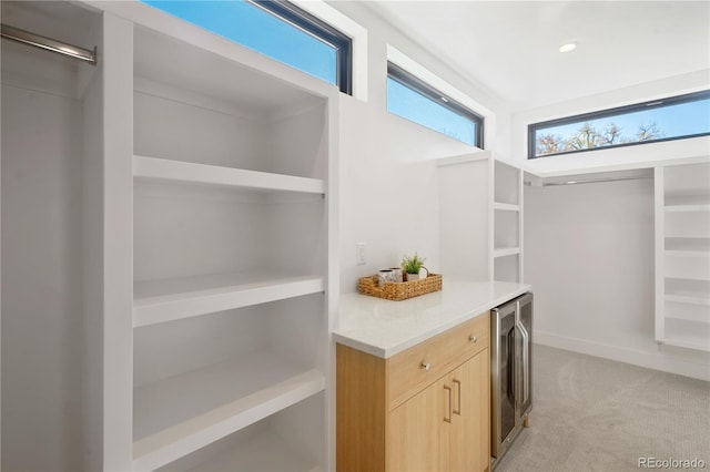 walk in closet with light colored carpet and beverage cooler