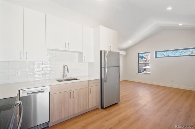 kitchen featuring sink, vaulted ceiling, light brown cabinetry, appliances with stainless steel finishes, and light hardwood / wood-style floors