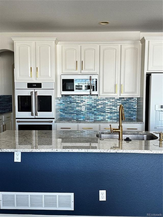 kitchen with sink, light stone counters, white cabinets, and white appliances