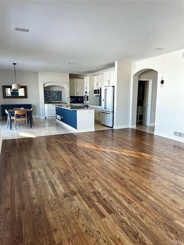 kitchen featuring high end refrigerator, wood-type flooring, hanging light fixtures, a center island with sink, and white cabinets