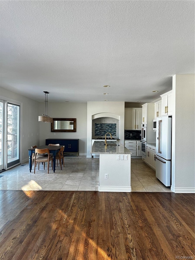 kitchen featuring sink, light hardwood / wood-style flooring, a kitchen island with sink, hanging light fixtures, and high end refrigerator