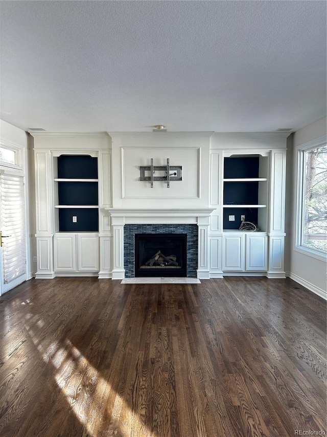 unfurnished living room featuring a tiled fireplace, built in shelves, dark hardwood / wood-style floors, and a textured ceiling