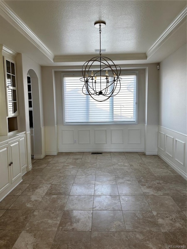 unfurnished dining area featuring a tray ceiling, ornamental molding, and a textured ceiling