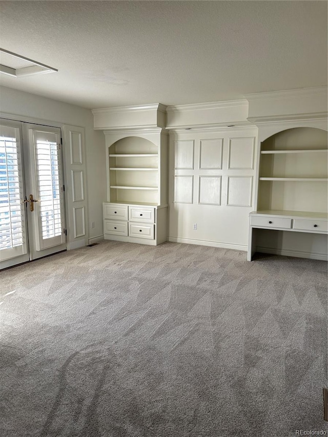 interior space featuring built in shelves, ornamental molding, light carpet, and a textured ceiling