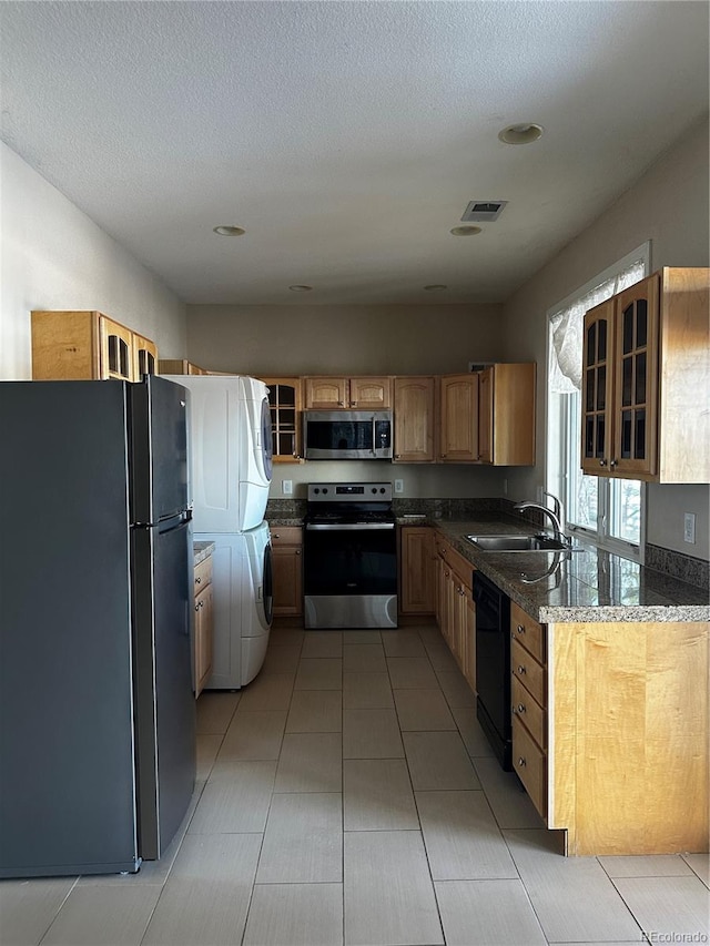 kitchen featuring stacked washer and dryer, sink, black appliances, a textured ceiling, and dark stone counters