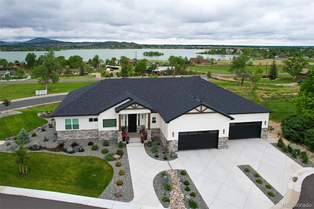 view of front facade with driveway, a shingled roof, stone siding, an attached garage, and a water and mountain view