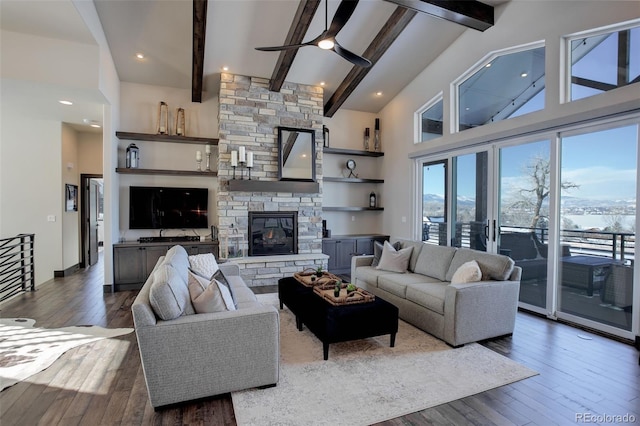 living area featuring a ceiling fan, a towering ceiling, dark wood-type flooring, a fireplace, and beam ceiling