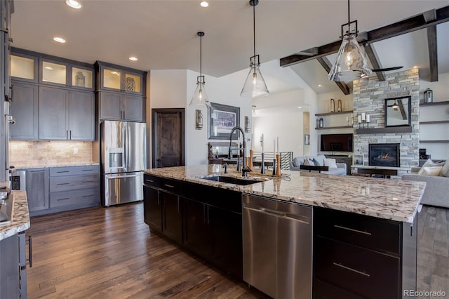 kitchen with a kitchen island with sink, dark brown cabinetry, stainless steel appliances, a sink, and glass insert cabinets