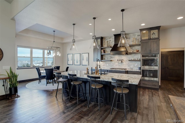 kitchen with premium range hood, appliances with stainless steel finishes, a tray ceiling, glass insert cabinets, and pendant lighting