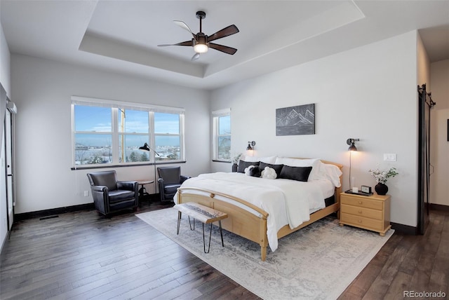 bedroom with dark wood-style floors, ceiling fan, a tray ceiling, and baseboards