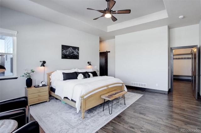 bedroom featuring dark wood-style floors, a raised ceiling, visible vents, ceiling fan, and baseboards