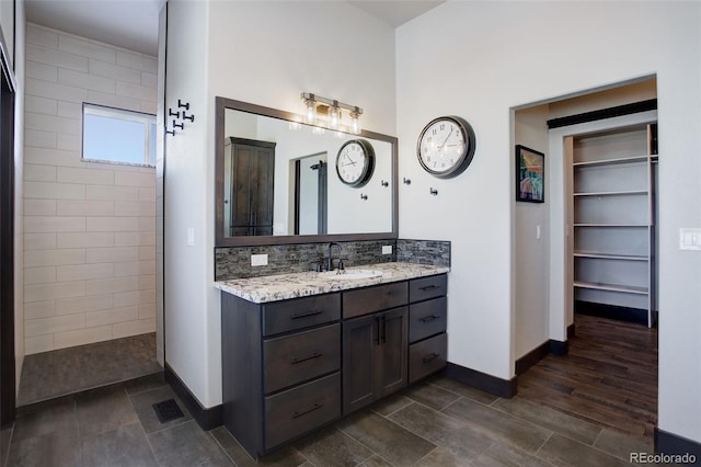 full bathroom featuring baseboards, decorative backsplash, a walk in closet, vanity, and a walk in shower