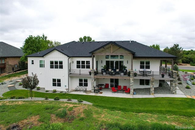 rear view of house with a shingled roof, a deck, a yard, a patio area, and board and batten siding