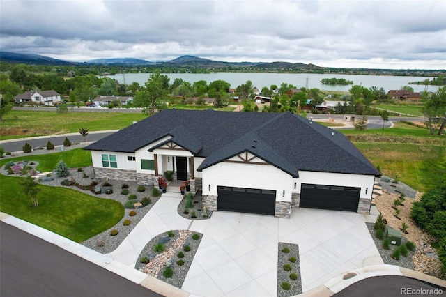 modern farmhouse featuring driveway, stone siding, roof with shingles, an attached garage, and a water and mountain view