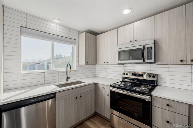 kitchen with appliances with stainless steel finishes, light countertops, a sink, and tasteful backsplash