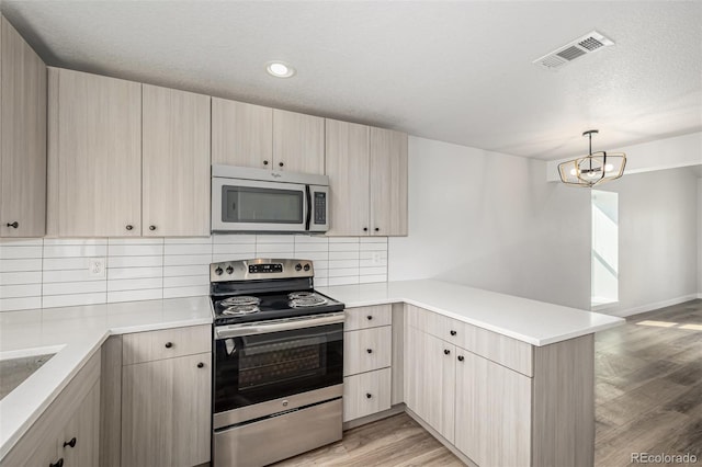 kitchen with visible vents, light wood-style flooring, a peninsula, stainless steel appliances, and backsplash