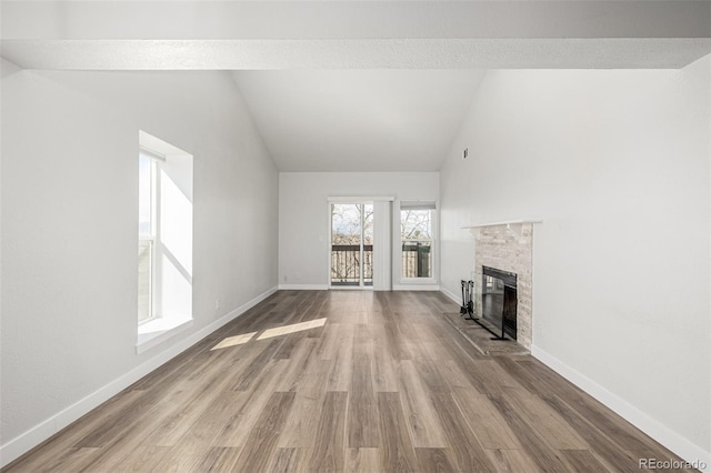 unfurnished living room featuring a fireplace with raised hearth, high vaulted ceiling, wood finished floors, and baseboards