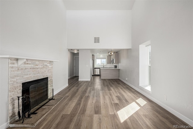 unfurnished living room with baseboards, visible vents, wood finished floors, a high ceiling, and a fireplace