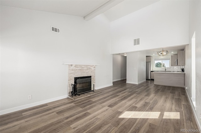 unfurnished living room featuring visible vents, a fireplace, beamed ceiling, and wood finished floors