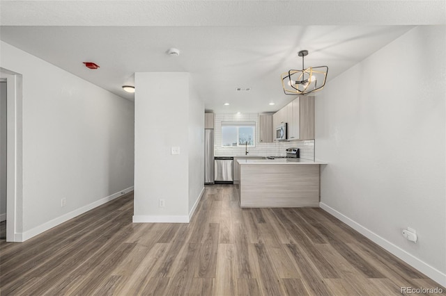 kitchen featuring decorative backsplash, appliances with stainless steel finishes, wood finished floors, a peninsula, and baseboards