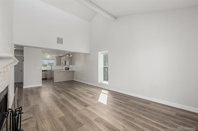 unfurnished living room featuring a fireplace, wood finished floors, visible vents, baseboards, and beamed ceiling