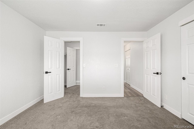 unfurnished bedroom featuring a textured ceiling, carpet floors, visible vents, and baseboards