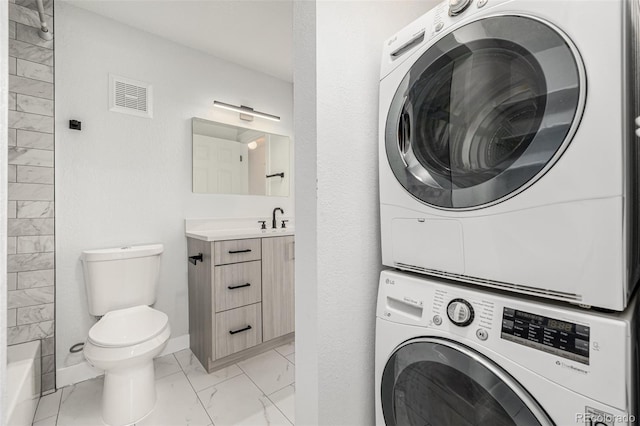 laundry room featuring visible vents, baseboards, marble finish floor, stacked washing maching and dryer, and a sink