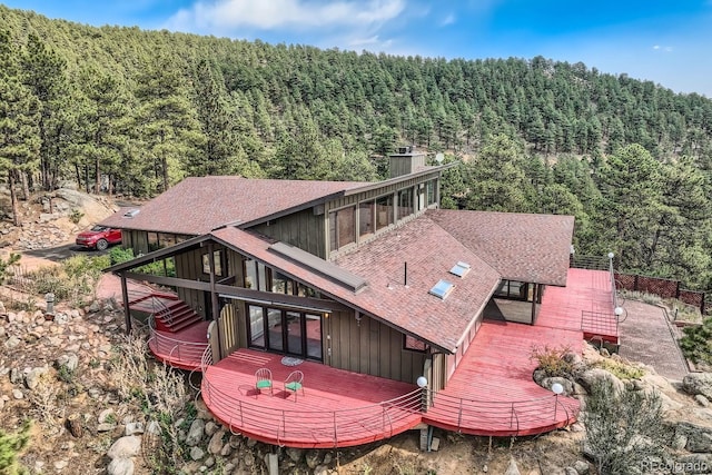 135 Poorman Rd, Boulder, CO 80302 - rear view of house with a wooded view, roof with shingles, board and batten siding, and a wooden deck