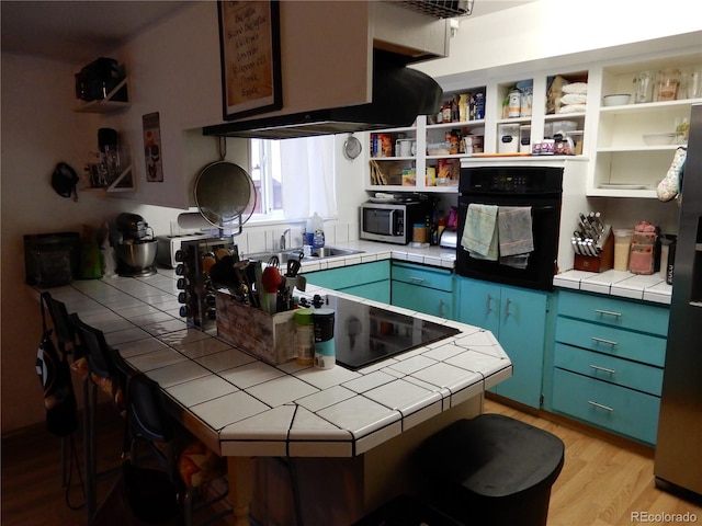 kitchen with tile counters, blue cabinets, stainless steel appliances, and light hardwood / wood-style flooring