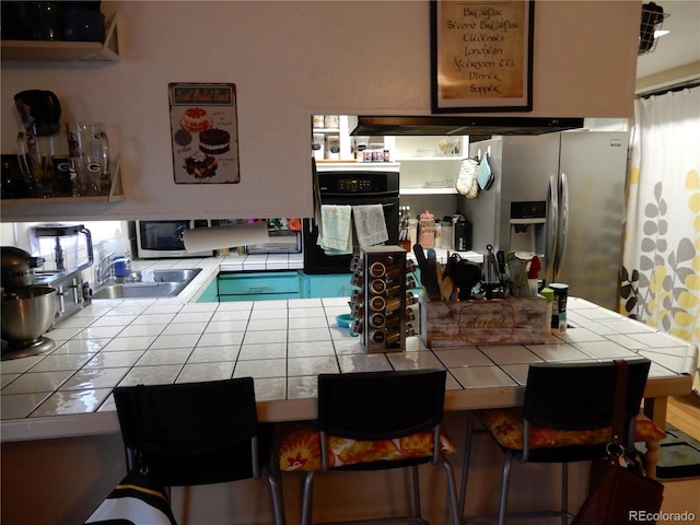 kitchen featuring tile countertops, oven, stainless steel fridge, and sink