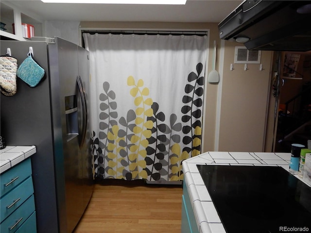 kitchen featuring blue cabinetry, tile counters, separate washer and dryer, stainless steel refrigerator with ice dispenser, and light hardwood / wood-style floors