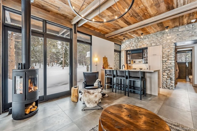 sitting room with a wood stove, tile patterned flooring, wood ceiling, and beamed ceiling