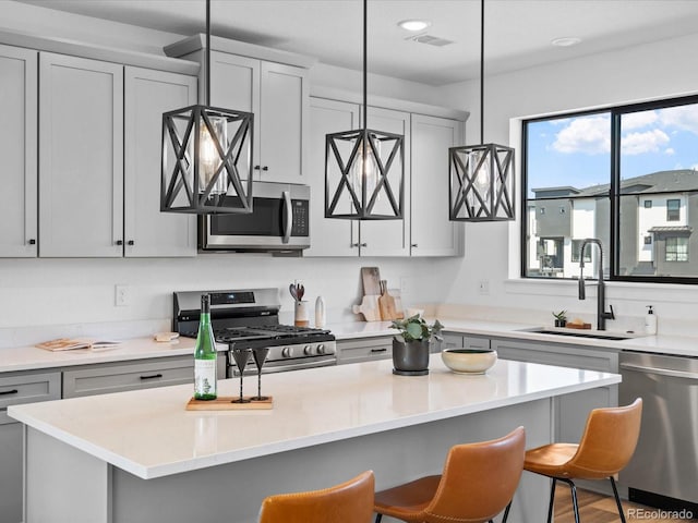 kitchen with a kitchen island, a breakfast bar, a sink, stainless steel appliances, and light countertops