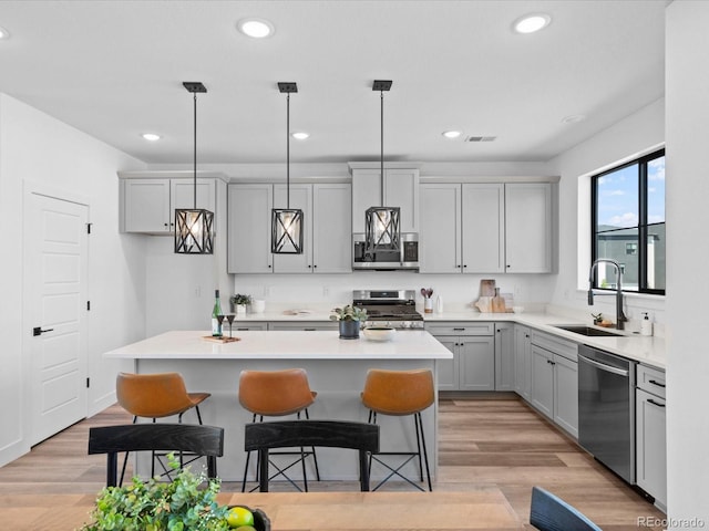 kitchen with gray cabinetry, a center island, a breakfast bar, stainless steel appliances, and a sink