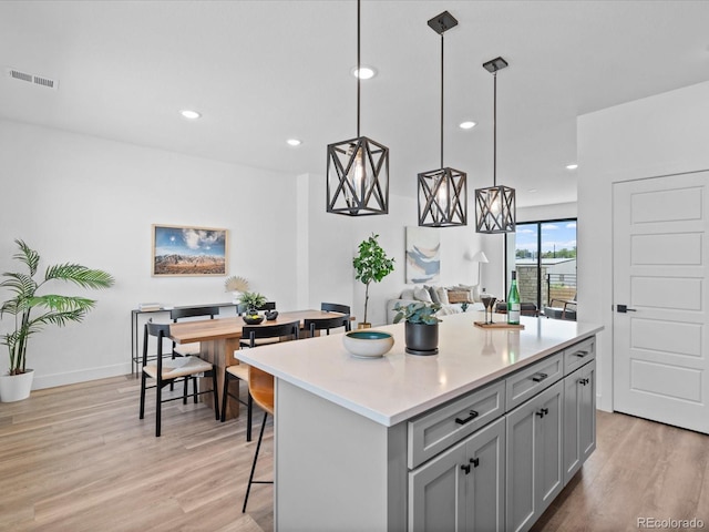 kitchen featuring visible vents, a kitchen island, gray cabinetry, light countertops, and light wood-type flooring