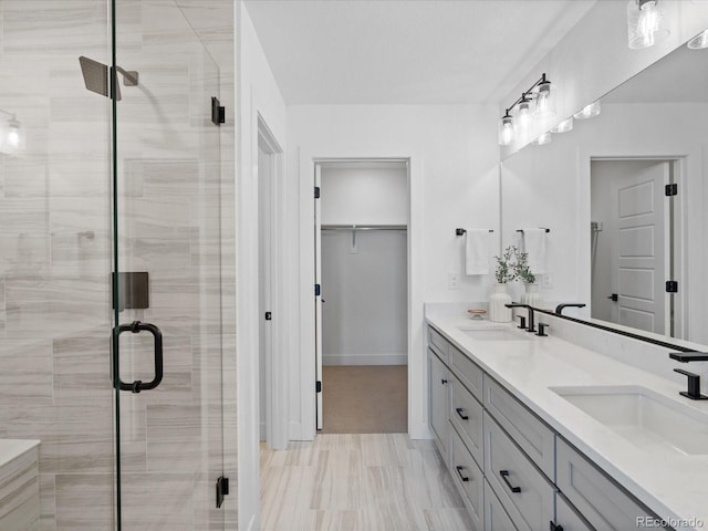 bathroom featuring a sink, a walk in closet, a stall shower, and double vanity