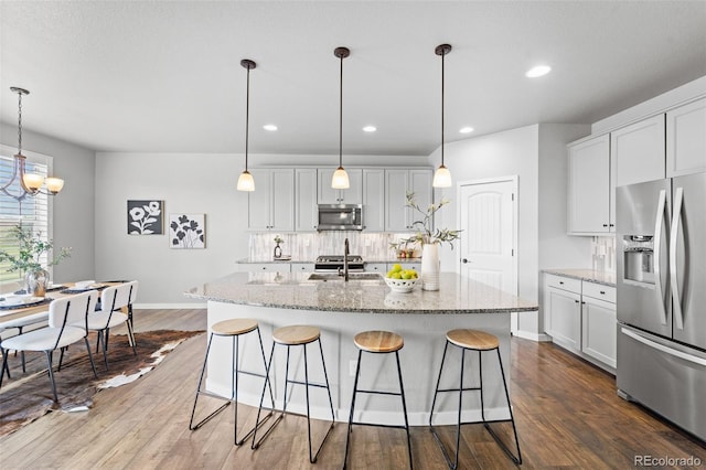 kitchen featuring appliances with stainless steel finishes, dark hardwood / wood-style flooring, light stone counters, a kitchen island with sink, and pendant lighting