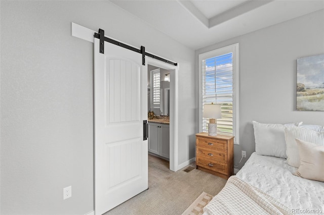 bedroom with a barn door, ensuite bathroom, and light colored carpet