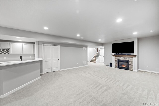 unfurnished living room featuring a stone fireplace and light carpet