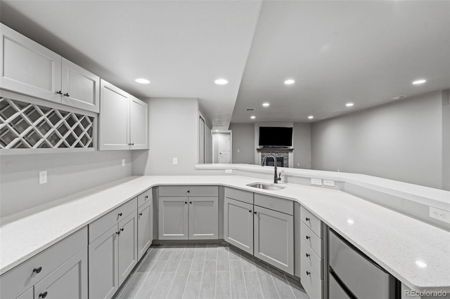 kitchen with gray cabinetry, light stone countertops, sink, a stone fireplace, and kitchen peninsula