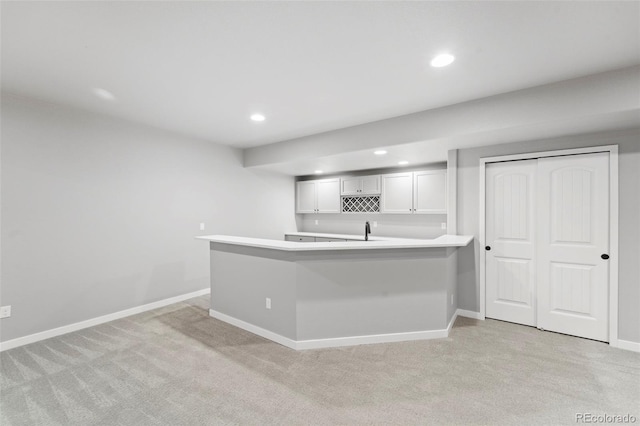 kitchen featuring white cabinetry, light colored carpet, kitchen peninsula, and sink