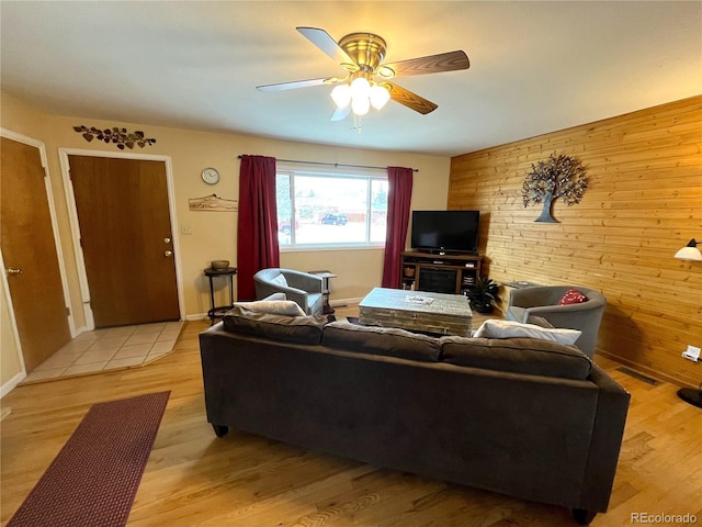 living area featuring visible vents, wood walls, a ceiling fan, and light wood-style floors