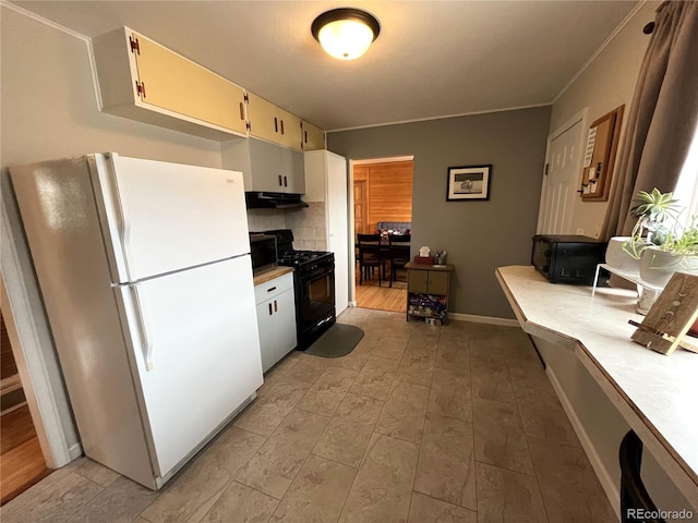 kitchen featuring under cabinet range hood, black gas stove, light countertops, freestanding refrigerator, and decorative backsplash