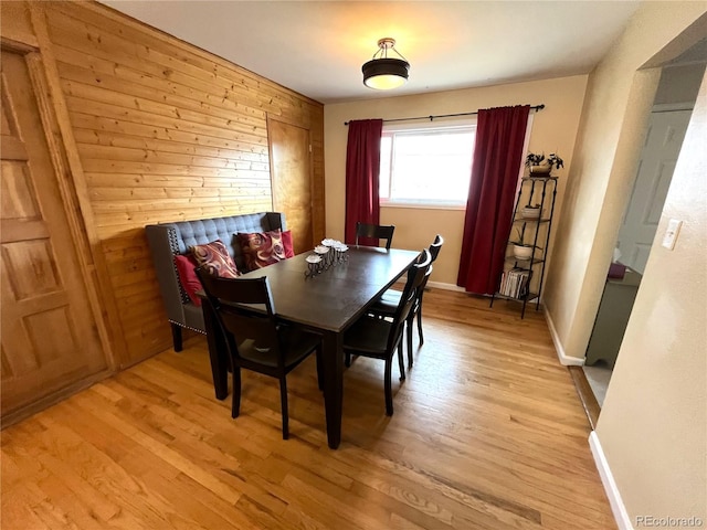 dining area featuring baseboards, wooden walls, and light wood finished floors