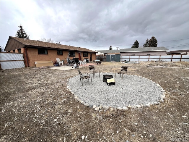 rear view of house featuring an outbuilding, a fire pit, brick siding, fence, and a patio area