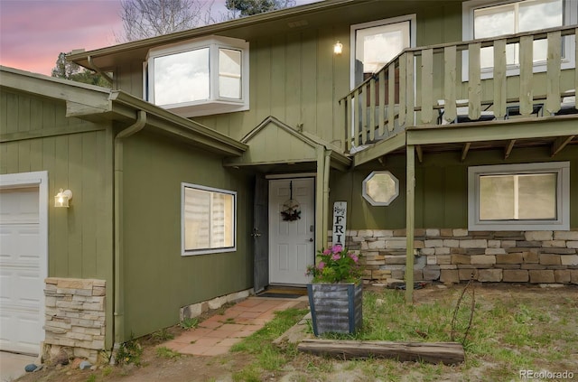 entrance to property featuring a balcony, stone siding, and a garage