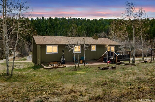 back of property featuring a wooden deck, a chimney, a yard, and a forest view