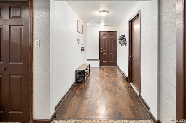 hall with baseboards, a textured wall, and dark wood finished floors